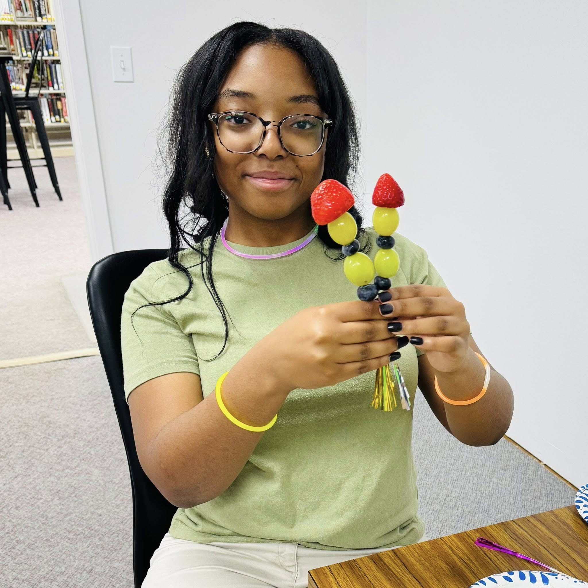 A girl holding two fruit kabobs.